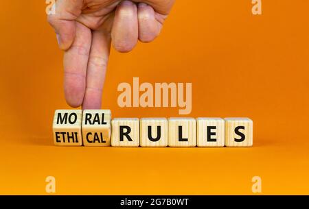 Ethical or moral rules symbol. Businessman turns wooden cubes and changes words 'ethical rules' to 'moral rules' on a beautiful orange background. Bus Stock Photo
