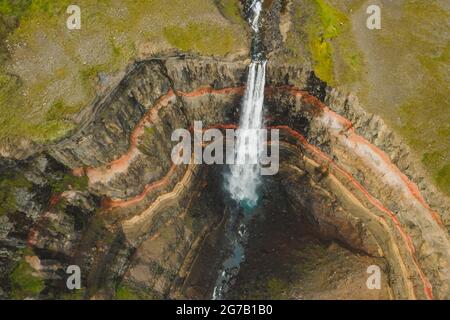 Aerial top down view of Hengifoss waterfall in East Iceland. The third highest waterfall in Iceland and is surrounded by basaltic strata with red layers of clay between the basaltic layers.