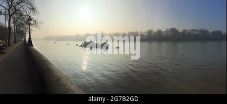 Misty winter morning on the river Thames in West London, England. View downriver priver from Chelsea Embankment looking towards Battersea Park and Albert Bridge. River Thames, Chelsea, London, England. Stock Photo