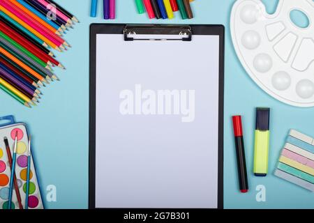 Art supplies for school painting and a blank sheet of paper on a clipboard on a blue background with copy space for text. Colorful pencils, markers Stock Photo