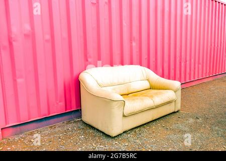 old leather sofa or settee or couch against pink corrugated metal siding in Alamogordo, New Mexico, United States Stock Photo