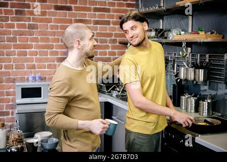Loving and caring handsome young man cooking tasty breakfast for husband Stock Photo