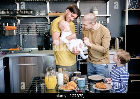 Curious boy looking at his cheerful fathers playing with baby boy in kitchen Stock Photo