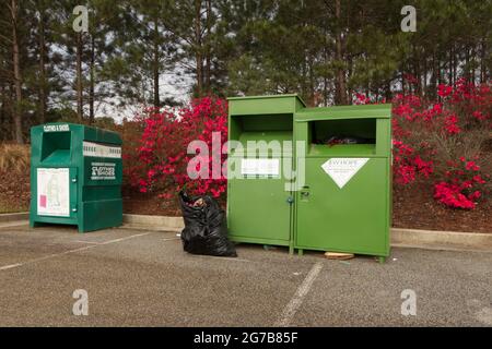 Augusta, Ga USA - 04 10 21: A row of donation drop off collection bins and a bag on the ground with red flowers in bloom Stock Photo