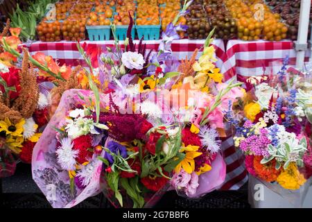 Bouquet of flowers on display for sale at farmer's market, with fruit and vegetables for sale in the background Stock Photo