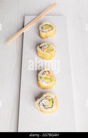 white plate with four sushi rolls with some wooden chopsticks, food in studio, delicious traditional dish Stock Photo