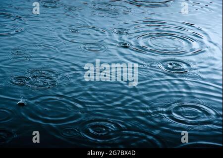 rain drops on the surface of water in a puddle with graduated shade of black shadow and reflection of blue sky Stock Photo