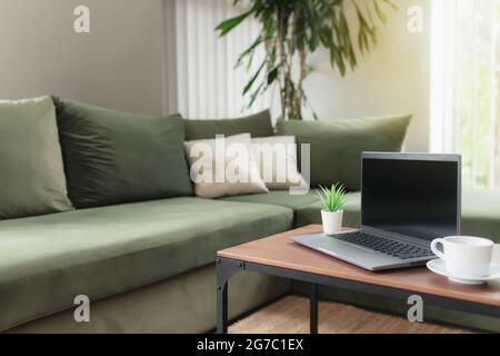 Work from home, workspace, desktop, remote work concept, gray thin laptop computer with black empty screen on brown wooden table with white cup of cof Stock Photo