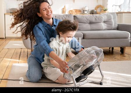 Caring mom relax has fun with child at home sit laugh together with son in front of fan ventilator Stock Photo