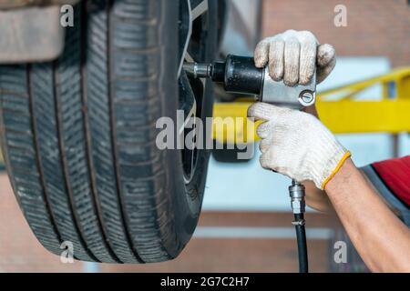 car service, maintenance and people concept - auto mechanic man with electric screwdriver changing tire at auto repair service center Stock Photo
