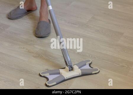 A young man in house slippers cleans the floor with a mop. Stock Photo