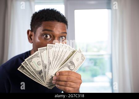 African American man holds up us currency to his face with eyes wide open, camera focuses on the money. Stock Photo