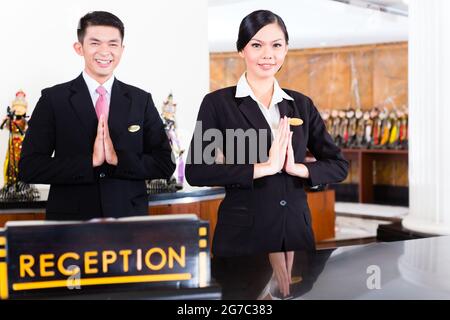 Chinese Asian reception team at luxury hotel front desk welcoming guests with typical gesture, a sign of good service and hospitality Stock Photo
