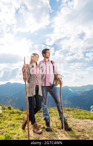 Hiking - Young couple standing on mountain summit in the Bavarian Alps enjoying the panorama in their leisure time or vacation Stock Photo