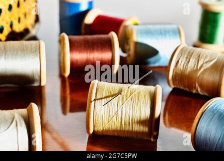 Spools of colored thread and needle on wooden table ,in the background sewing basket Stock Photo