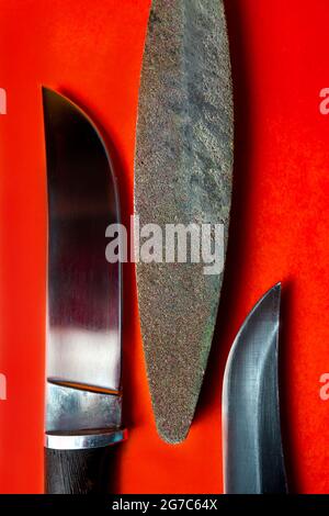 two handmade knives and a bar for sharpening on a red background. Stock Photo