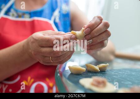 a woman in the kitchen prepares dumplings from dough and minced meat. Stock Photo