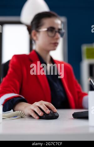 Focus on hand of businesswoman holding computer mouse working in corporate office. Entrepreneur clicking on device with wireless connection doing financial analysis. Close up shot of woman on mouse. Stock Photo