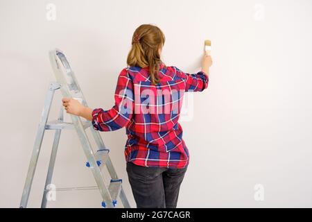 Woman paints walls with white paint standing on a ladder, copy space Stock Photo