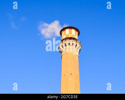 Tower made of bricks with a chimney from which white smoke comes out in a blue sky. Stock Photo