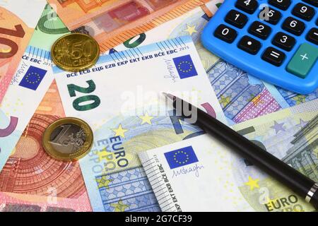 An financial still life with a mixture of Euro currency notes, coins, calculator, and a pen.