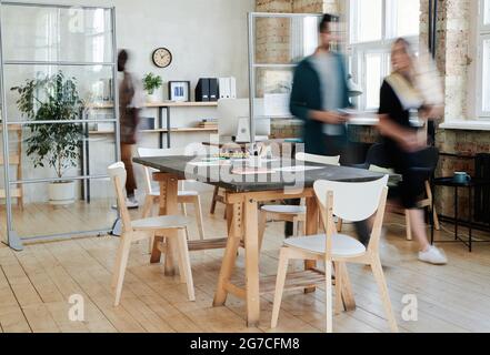 Blurred motion of business people cooperating together at office with conference table standing in the centre Stock Photo