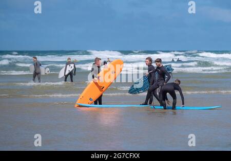 A group of friends carrying their hired surboards standing in the sea at Mawgan Porth on a Cornish staycation surfing holiday in the UK. Stock Photo