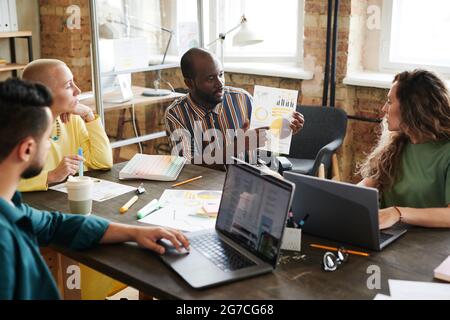 African businessman pointing at financial document and discussing it together with his colleagues during business meeting at office Stock Photo