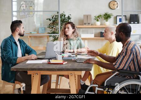 Young businesswoman sitting at the table together with her partners discussing and working in team during a business meeting Stock Photo