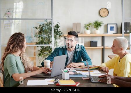 Male business leader sitting at the table and talking to his employees during business meeting at office Stock Photo