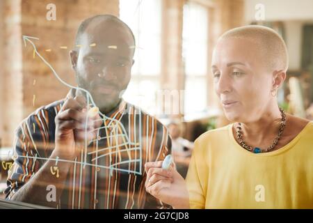 Business people drawing graphs together on glass wall and examining financial degrees during presentation at office Stock Photo