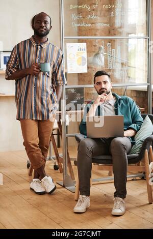 Portrait of two young designers looking at camera while working with laptop at office Stock Photo