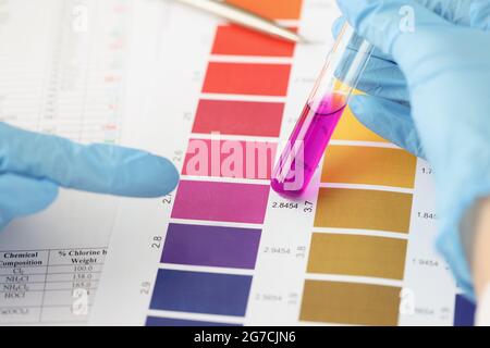 Scientist compares purple liquid in test tube to color bar Stock Photo