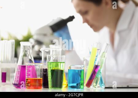 Multi-colored liquid in flasks in background woman scientist looks through microscope Stock Photo