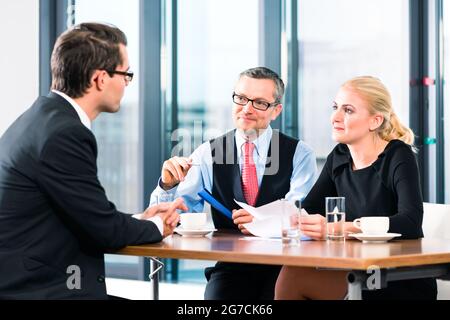 Business - young man in an Job interview, signs his employment contract with boss and his female assistant in their office Stock Photo