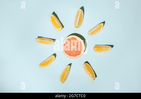 Orange slices arranged around a red grapefruit on a blue background. Stock Photo