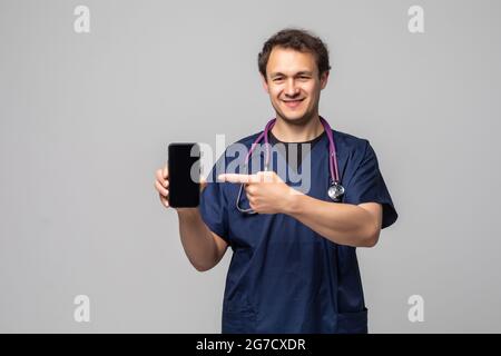 Young doctor showing a phone and pointing isolated on white background Stock Photo