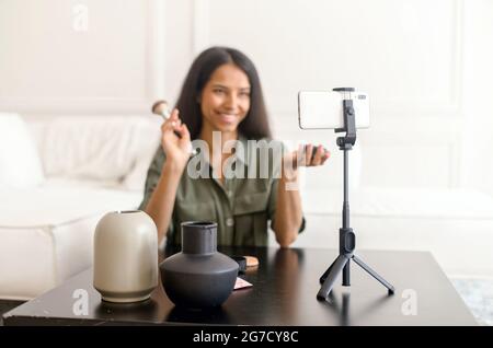 Charming glamorous indian woman beauty vlogger doing makeup in front of smartphone on the tripod and sharing on social media, streaming live video tutorial, online influencer girl recording content Stock Photo
