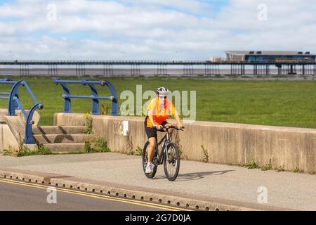 Southport, Merseyside.  Uk Weather. 13 July 2021: Early sunshine and warming temperatures reach 20C, as local residents take light exercise on the resort seafront promenade. Activities on the Coastal road as the dune habitat & grassing of the sands (Accretion), appears to extend across to the Fylde Coast.  The Sefton coast is struggling to repel two invaders – the sea and tough grasses sprouting over the beach which will eventually engul the pier as sand dunes form. Credit; MediaWorldImages/AlamyLiveNews Stock Photo