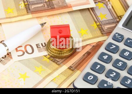 A house sitting on coins, on Euro currency notes, with a pen and calculator. Stock Photo
