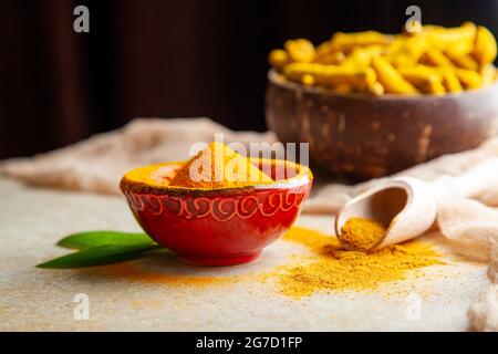 Dried turmeric powder with leaves and roots in coconut shell bowl. Stock Photo
