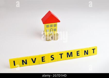 A house sitting on coins with a banner in front with the words ' INVESTMENT ' Stock Photo