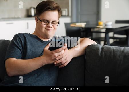 Young man with down syndrome using cellphone while sitting on couch at home Stock Photo