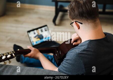 Young man with down syndrome playing guitar while using laptop at home Stock Photo