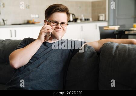Young man with down syndrome talking on cellphone while sitting at home Stock Photo