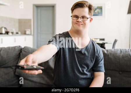 Young man with down syndrome using remote control while sitting on couch at home Stock Photo
