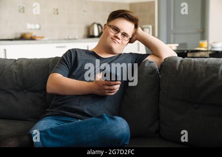 Young man with down syndrome using cellphone while sitting on couch at home Stock Photo