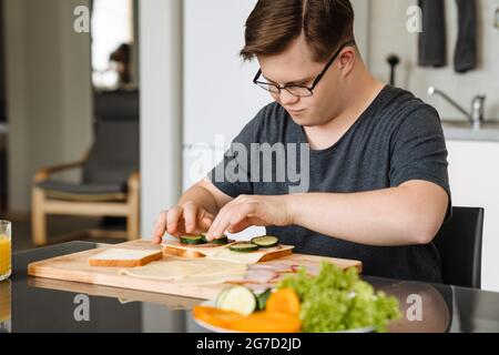 Young man with down syndrome making sandwiches in kitchen at home Stock Photo