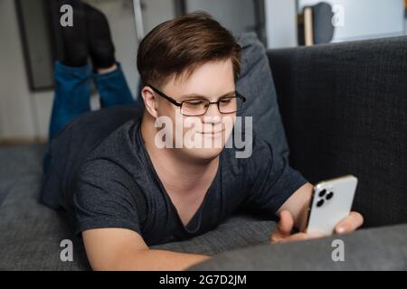 Young man with down syndrome using cellphone while lying on couch at home Stock Photo
