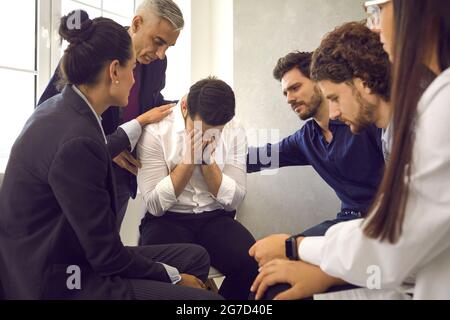 Compassionate people in group therapy comforting and supporting distraught young man Stock Photo